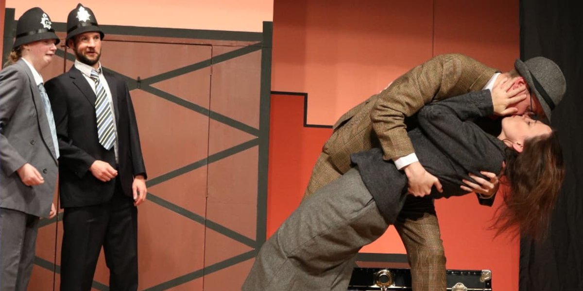 A scene from Brightlight Theatre's production of The 39 Steps. A couple kiss whilst two shocked policemen watch.